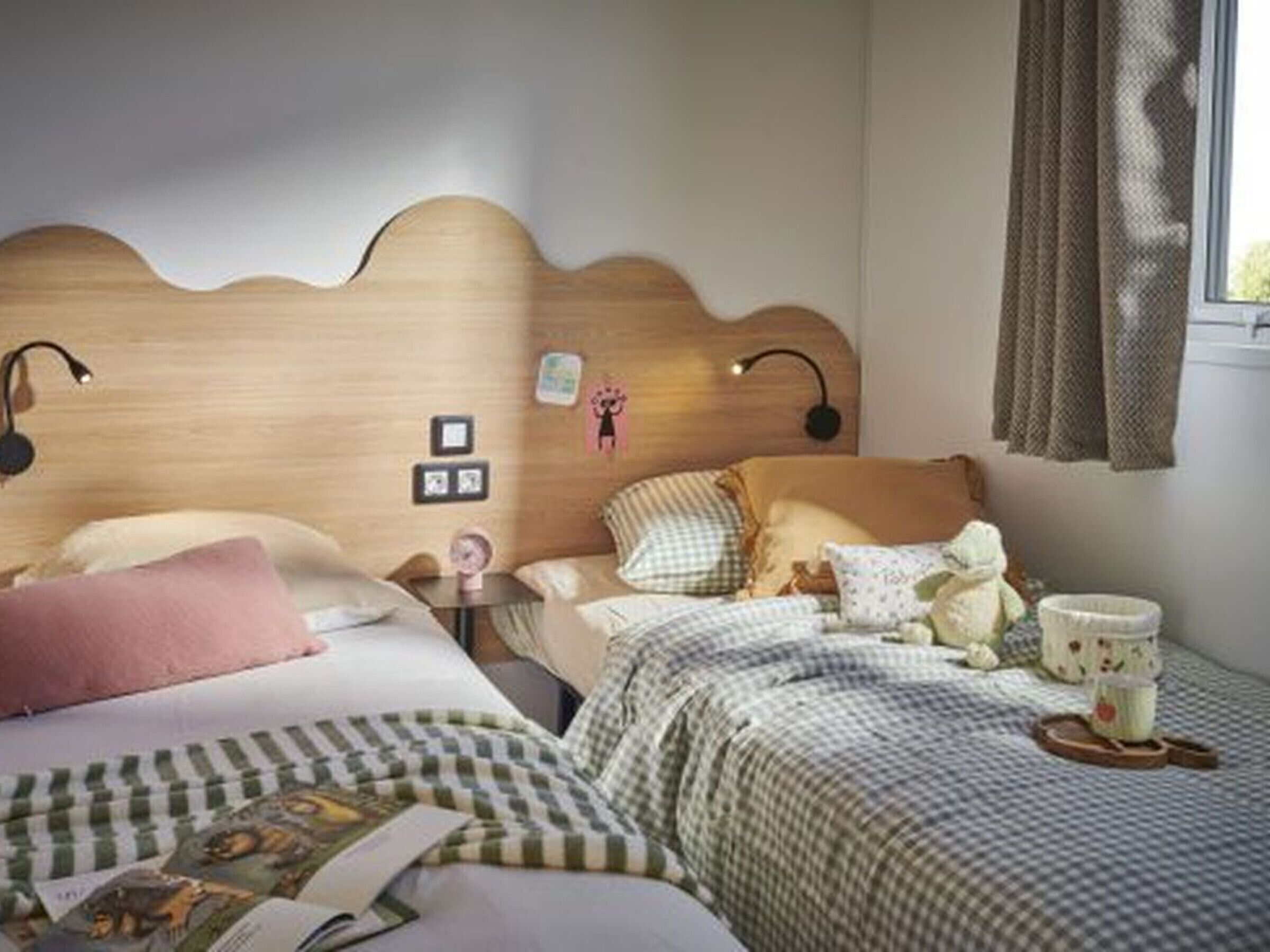 Un dormitorio con dos camas, cabecero de madera, lámparas de noche, mesitas de noche y una ventana con cortinas.