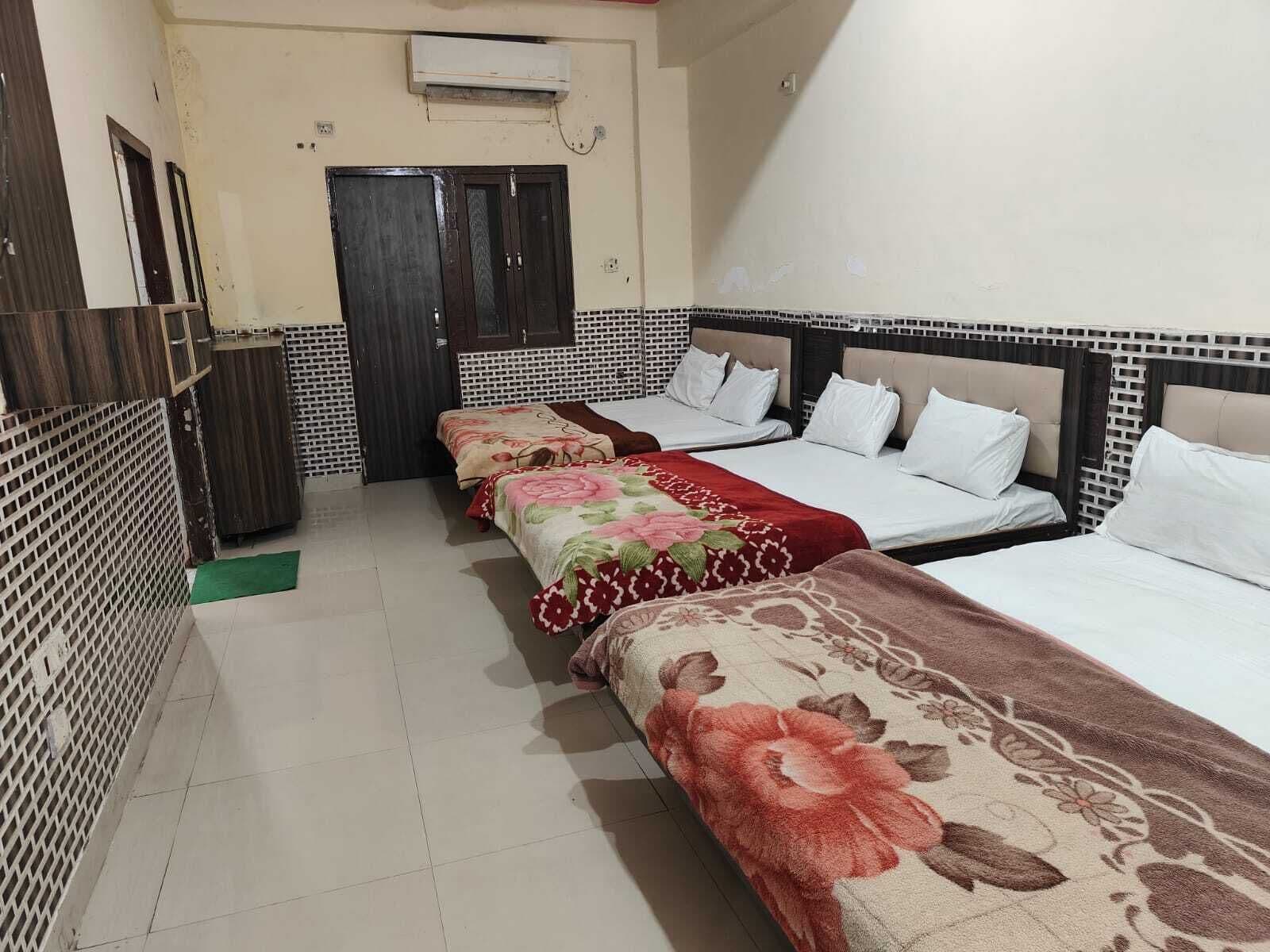 A hotel room with three beds, a tiled floor, a door, and an air conditioning unit.