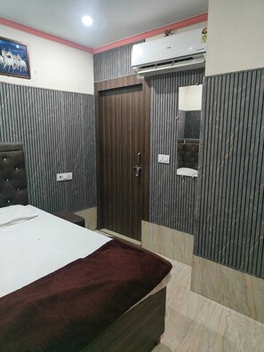 A bedroom with a bed, a wardrobe, an air conditioning unit, and a mirror. - Ramkrishna Bhawan Hotel (Mathura)