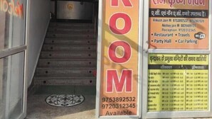 L’entrée d’un hôtel, avec un escalier menant aux chambres. Des affiches sont accrochées aux murs, dont une avec le mot « CHAMBRE » et une autre avec une liste des équipements disponibles, comme un restaurant et un parking.