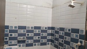 Une petite salle de bain simple, équipée d’un WC, d’un lavabo et d’une douche. Les murs sont recouverts de carreaux aux motifs bleus et blancs.