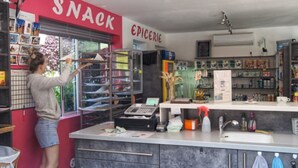 A snack bar with a counter, shelves with various items, and a person arranging items on the counter. - Mobile Home with Terrace - 4 people (Saint-Rome-de-Tarn)