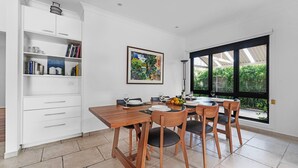 Un coin repas avec une table et des chaises en bois, une bibliothèque et une grande fenêtre donnant sur un paysage verdoyant.