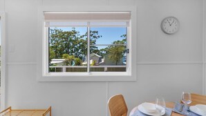 Zona pranzo con finestra, orologio e vista su case e alberi.