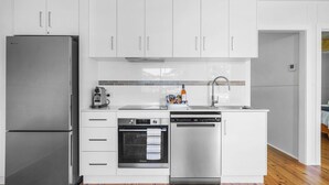 Una cucina moderna con mobili bianchi, un frigorifero in acciaio inossidabile, forno integrato, lavastoviglie e macchina da caffè.