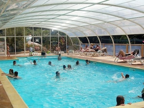 An indoor swimming pool with a glass ceiling, surrounded by lounge chairs and a poolside area. - Mobile home with terrace in Binic for 4 people (Binic)