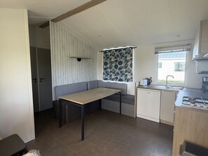 A compact kitchen with a dining area, a window with a curtain, and a view of the outside.