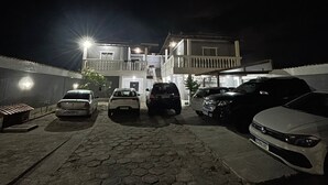 Un área de estacionamiento nocturno con varios coches aparcados frente a un edificio con balcones.