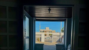 Un pasillo estrecho con suelo de baldosas que conduce a un espacio al aire libre con un banco y vistas a un edificio y coches aparcados.