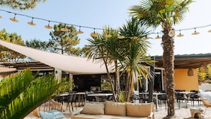 An outdoor seating area with a sofa, round table, and chairs, surrounded by palm trees and string lights. - Mobile home with terrace in Saint-Jean-de-Monts (Saint-Jean-de-Monts)