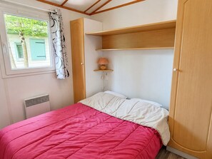 Et soveværelse med seng, et vindue med gardiner, en reol med lampe og et klædeskab.