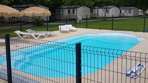 Ein Swimmingpool mit einem umzäunten Bereich, Liegestühlen und strohgedeckten Sonnenschirmen.