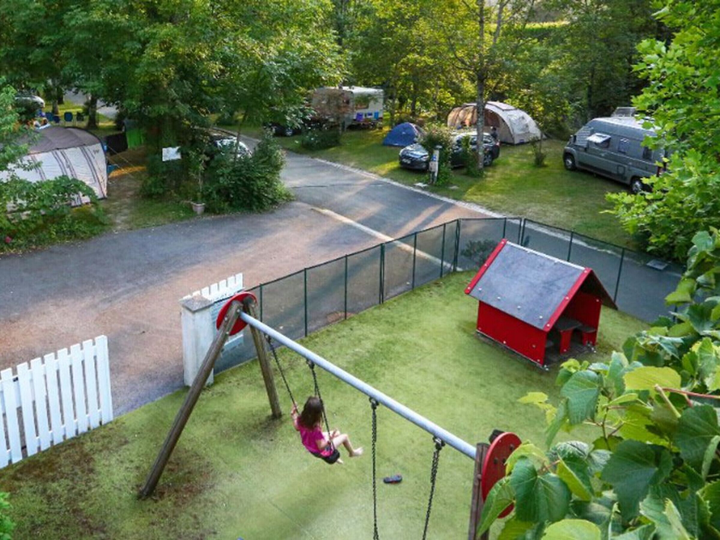 A playground with a swing set, a red playhouse, and a fenced area.