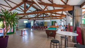 Et rummeligt indendørs område med poolbord, siddepladser og bar.
