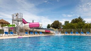 Una piscina con tobogán de agua, sillas de descanso y una torre de salvavidas.