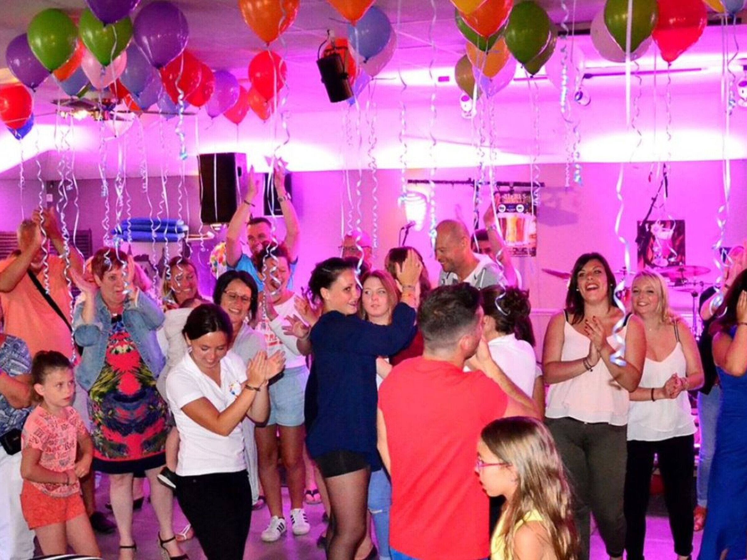A group of people in a room with a stage and musical equipment, suggesting a social event or party.