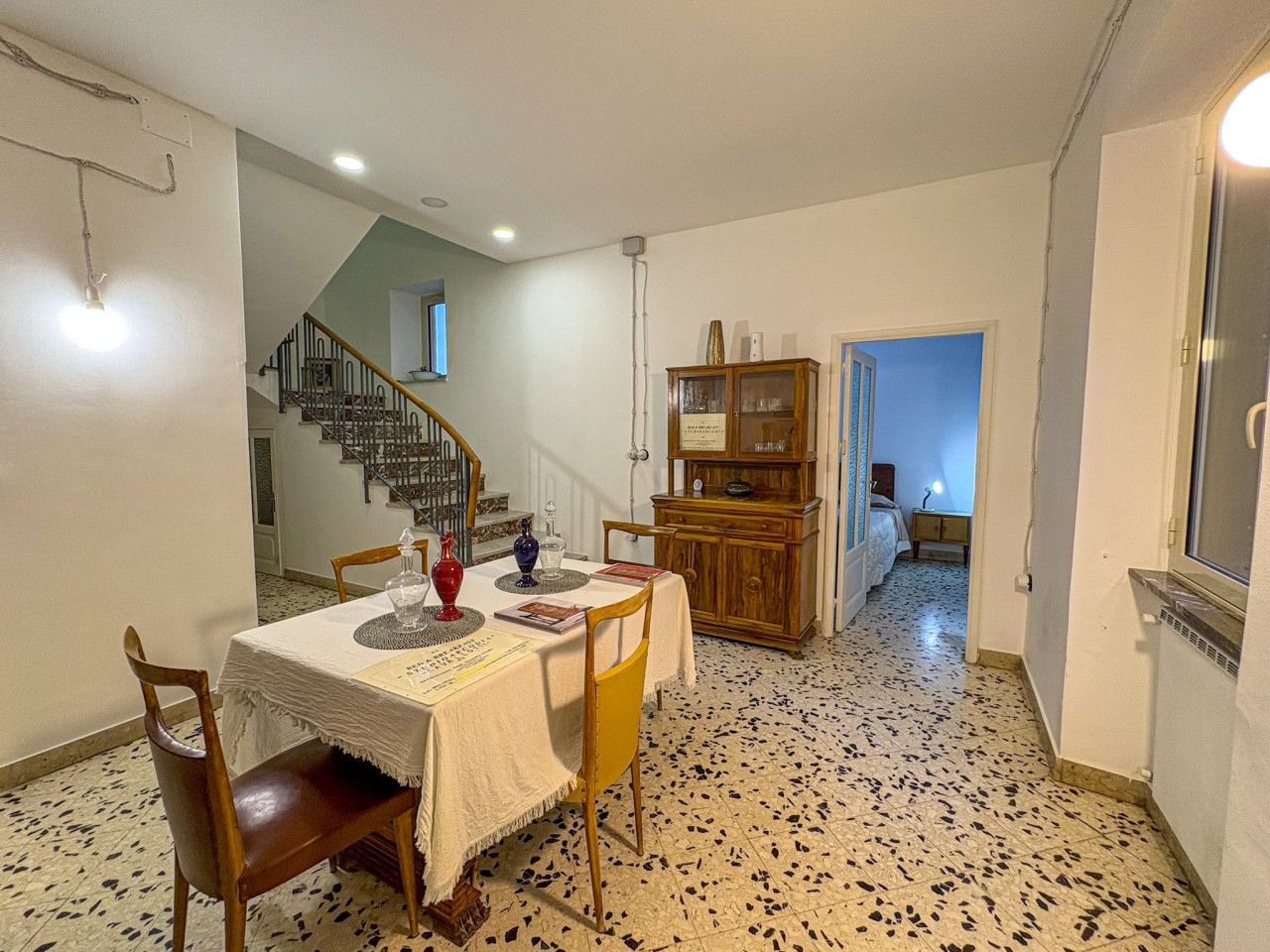 Ein Essbereich mit Tisch für zwei, eine Treppe, eine Holzkommode und ein Zimmer mit Bett.