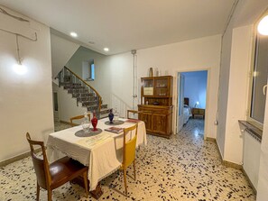 A dining area with a table set for two, a staircase, a wooden cabinet, and a room with a bed. - B&B StudioArcodia - Camera Matrimoniale (San Marco D`alunzio)