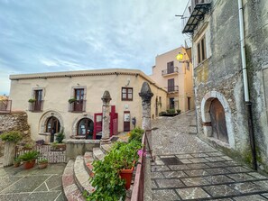 Una calle estrecha con edificios que tienen puertas y ventanas de arco, escalones de piedra y plantas en macetas.