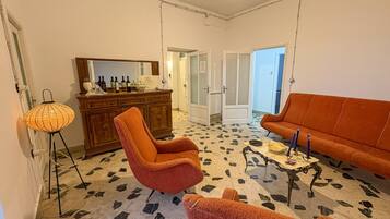 Ein Zimmer mit einem gemusterten Boden, einer Holzkabine, einem roten Sessel, einem orangefarbenen Sofa und einem kleinen Tisch mit Kerzen.