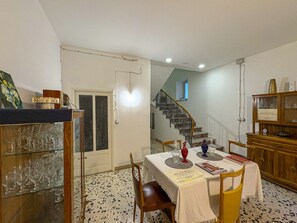 A dining area with a table set for four, a staircase in the background, and a wooden cabinet with glassware. - B&B StudioArcodia - Camera Matrimoniale (San Marco D`alunzio)