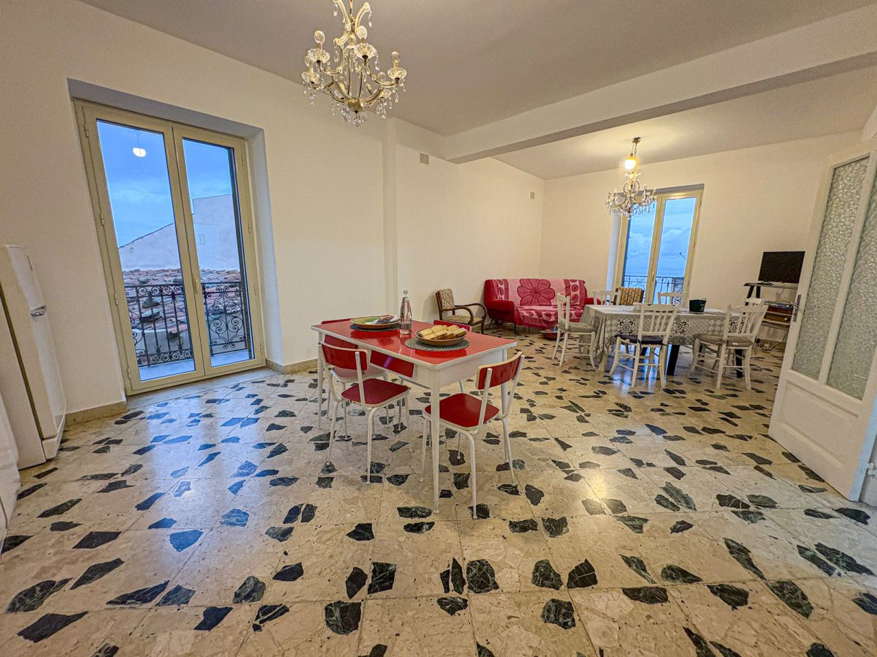 Un coin repas avec une table et des chaises rouges, un lustre et une vue à travers une porte vitrée.