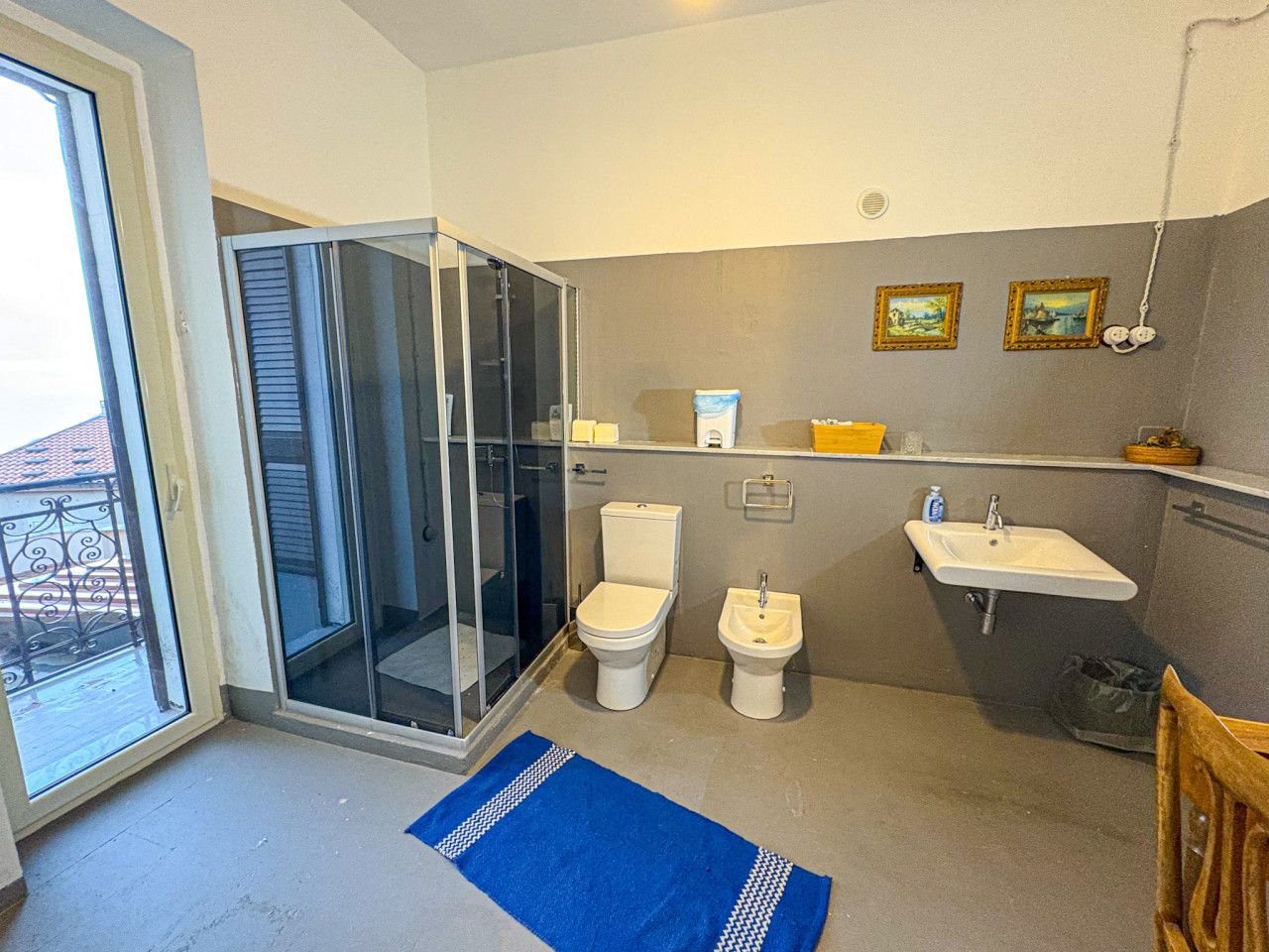 Ein Badezimmer mit Duschkabine aus Glas, zwei Toiletten, einem Waschbecken und einem kleinen Ablagebereich für Pflegeartikel.