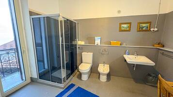 Ein Badezimmer mit Duschkabine aus Glas, zwei Toiletten, einem Waschbecken und einem kleinen Ablagebereich für Pflegeartikel.