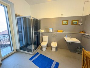 Un baño con cabina de ducha de vidrio, dos inodoros, un lavabo y una pequeña repisa con artículos de aseo.