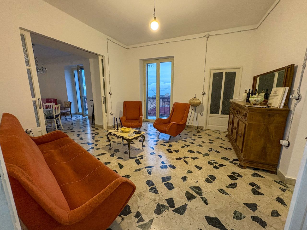 Een woonkamer met twee oranje fauteuils, een bijzettafeltje en een houten kast. De vloer heeft een betegeld patroon.