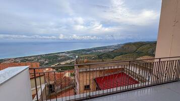 Ein Balkon mit einer roten Matte und Blick auf das Meer sowie eine in der Ferne liegende Stadt.