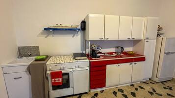Eine kleine Küche mit weißen Schränken, einer roten Arbeitsplatte, einem Herd, einer Spüle und einem kleinen Kühlschrank.