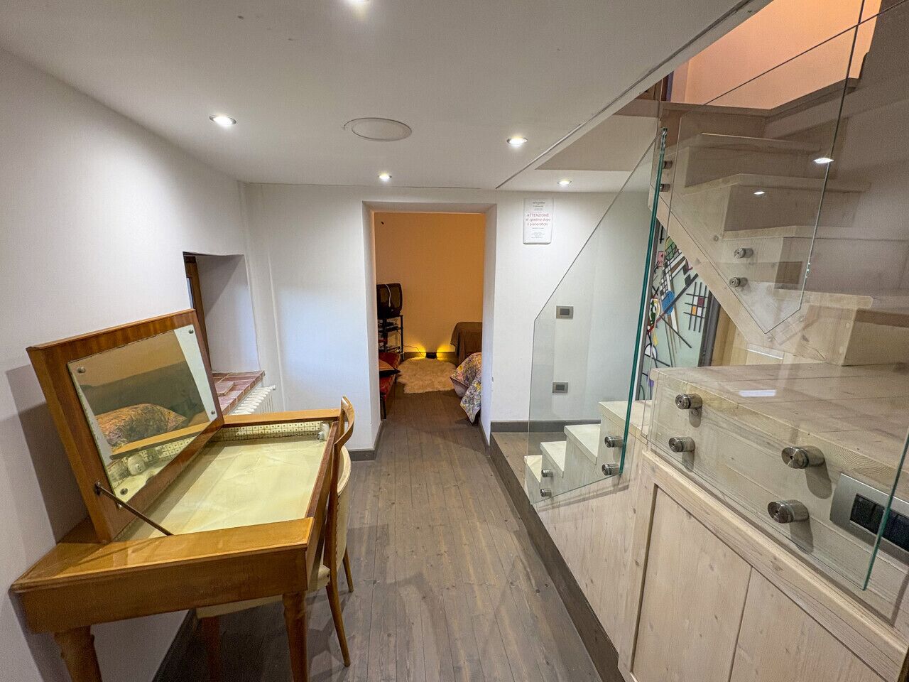 A hallway with a wooden display case, a glass staircase, and a door leading to another room.