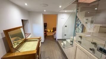 A hallway with a wooden display case, a glass staircase, and a door leading to another room.