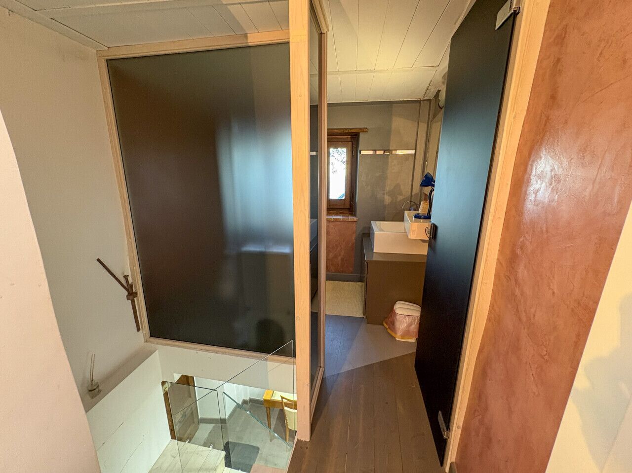 A room with a large sliding door, a small bathroom with a sink, and a wooden floor.
