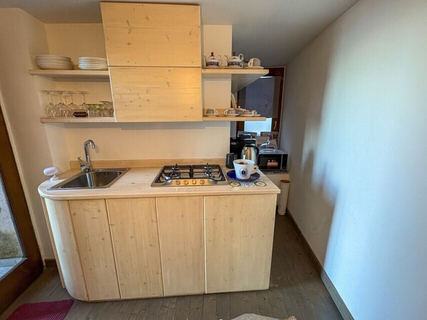 Una cocina compacta con estufa a gas, lavamanos y armarios de madera.