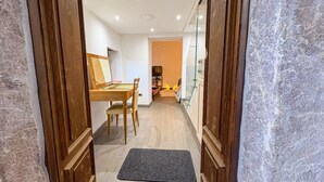 Un pasillo que conduce a un comedor con una mesa y sillas de madera, una alfombra en el suelo y un ventanal a la derecha.