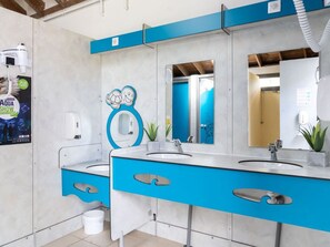 A bathroom with two sinks, a mirror, a towel dispenser, and a poster advertising an aquarium show.
