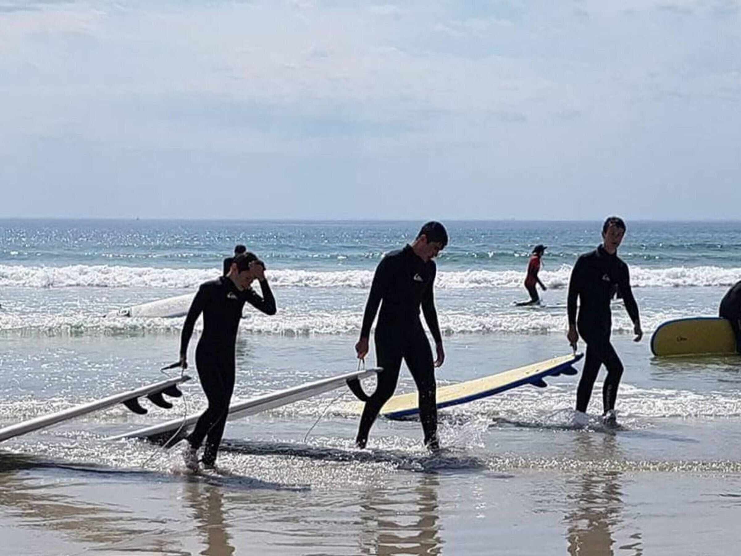 A beach scene with people in wetsuits walking with surfboards.