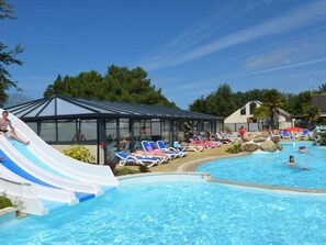 Piscina con tobogán de agua, sillas de descanso y una zona de estar techada.
