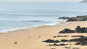 Uma praia com vista clara para o oceano e colinas ao longe.