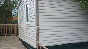 A wooden deck leading to a white building with a window and a number sign '82' on the side. - PMR Mobile Home with Terrace in Roquebrune-sur-Argens (Roquebrune-sur-Argens)