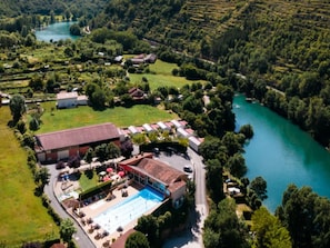 Vista aérea de un hotel con piscina, rodeado de abundante vegetación y un río.