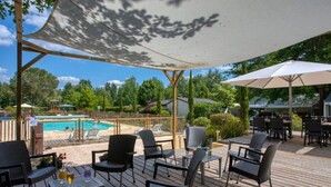 An outdoor deck with a pool, lounge chairs, and umbrellas. - 27m² Mobile Home with Terrace in Groléjac (Groléjac)