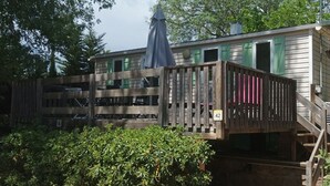 A two-story wooden cabin with a covered outdoor area and a wooden deck. - 23m² Mobile Home for 4 with Raised Terrace (Roquebrune-sur-Argens)
