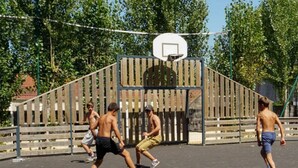 Ein Basketballplatz mit hölzernem Zaun und Bäumen im Hintergrund.