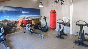 Ein Fitnessraum mit Trainingsgeräten, einem Sandsack und einem Wandbild eines Vans am Strand.