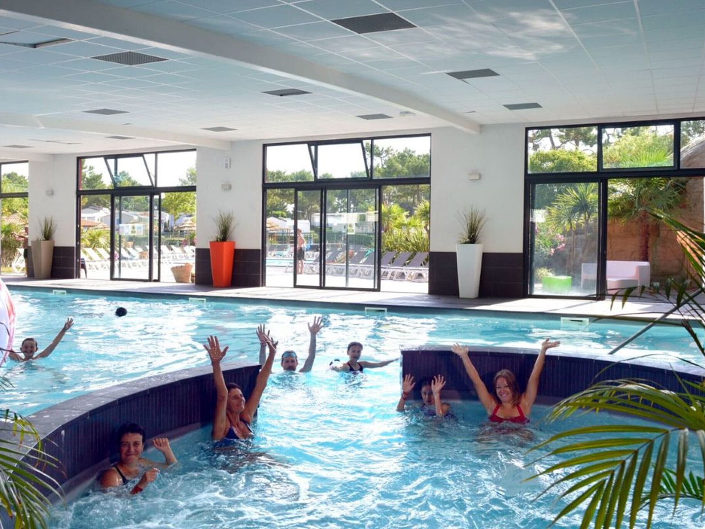 Une piscine intérieure offrant une vue dégagée sur l’extérieur, de grandes fenêtres et des plantes en pot disposées autour de la piscine.