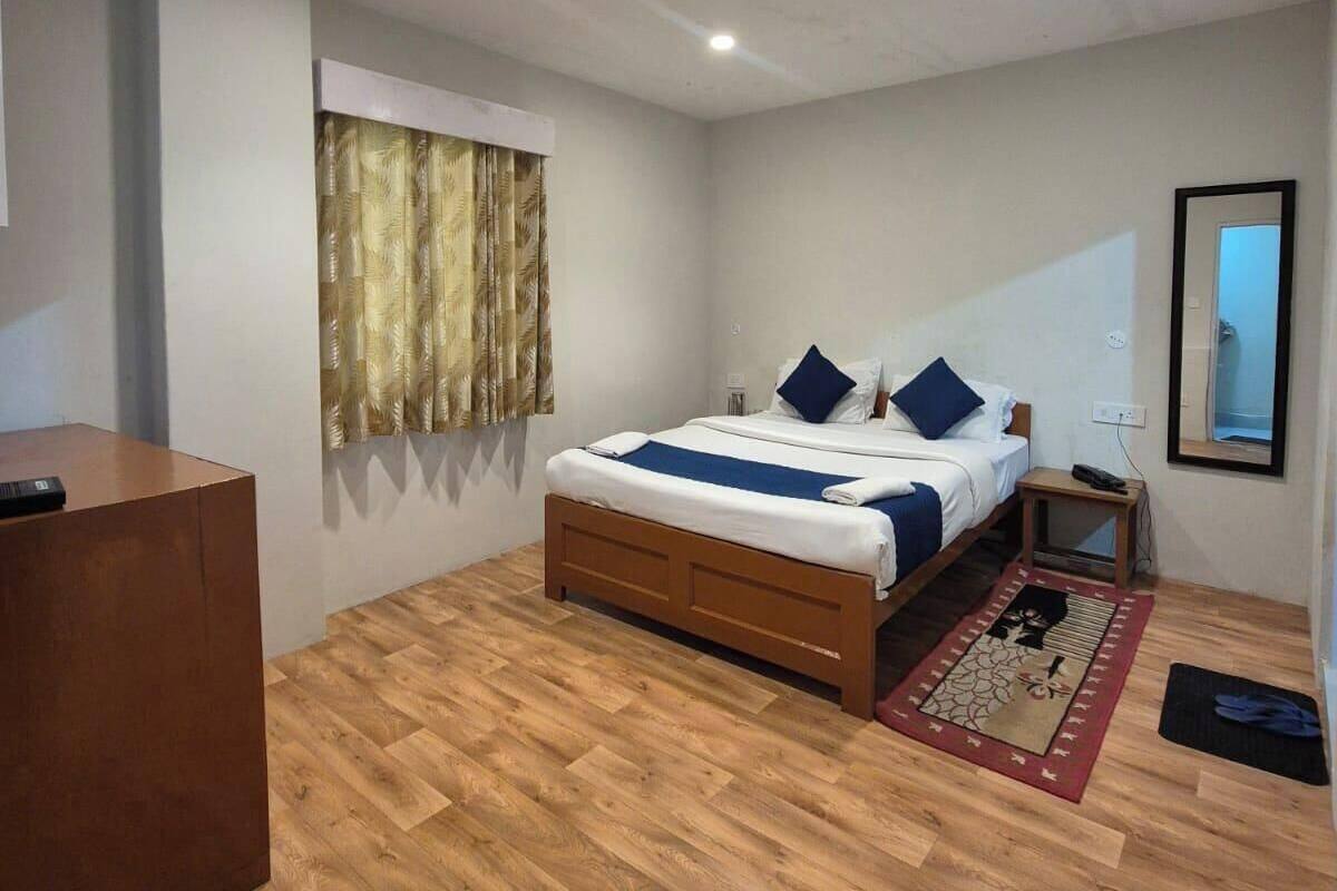 A bedroom with a wooden bed, a desk, a window with curtains, a nightstand, and a mirror.
