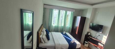 A hotel room with a bed, a desk, a television, and a window with curtains.